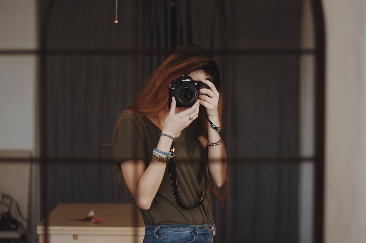 A female photographer capturing a self-portrait with a DSLR camera in an indoor setting.